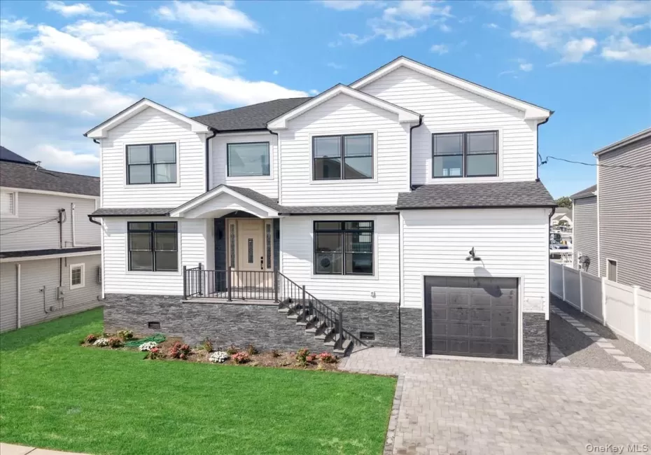 White siding exterior with black-framed windows, stone accent foundation, and a paver driveway White siding exterior with black-framed windows, stone accent foundation, and a paver driveway