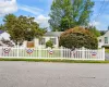 White picket fence enclosing the front yard, featuring a mailbox, mature landscaping, and a pale yellow exterior with green shutters White picket fence enclosing the front yard, featuring a mailbox, mature landscaping, and a pale yellow exterior with green shutters