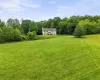 Expansive green lawn surrounds the property, featuring a traditional style home with a light-colored facade and dark shutters, set against a backdrop of mature trees Expansive green lawn surrounds the property, featuring a traditional style home with a light-colored facade and dark shutters, set against a backdrop of mature trees