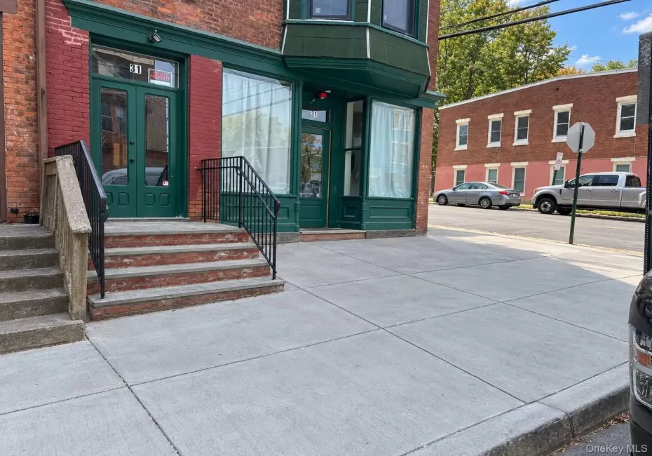 Brick facade building featuring a green double-door entry, a bay window, and a concrete walkway Brick facade building featuring a green double-door entry, a bay window, and a concrete walkway