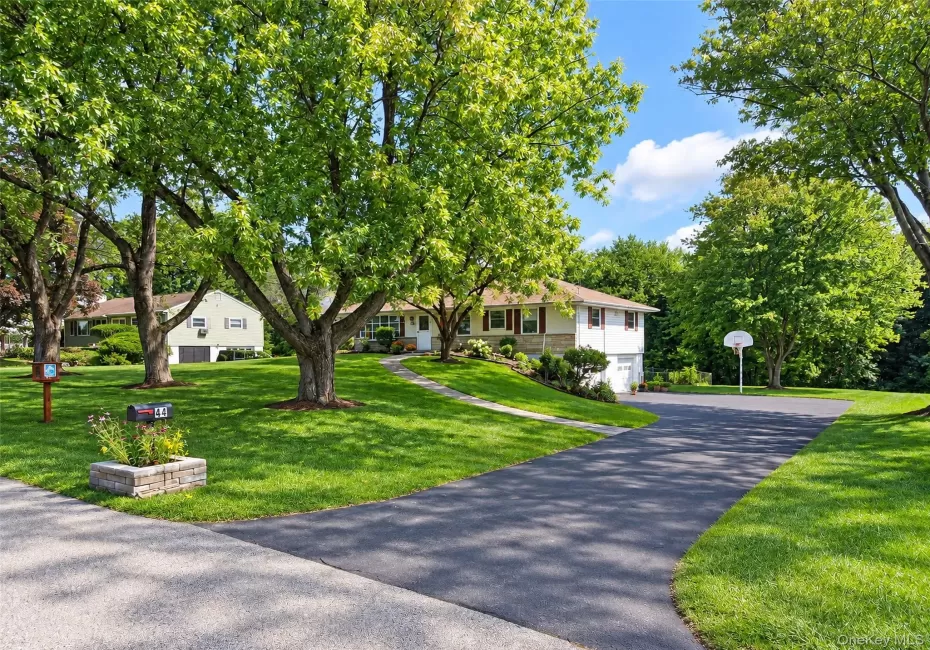 Split-level residence featuring a white and stone exterior, attached garage, paved driveway, and mature landscaping Split-level residence featuring a white and stone exterior, attached garage, paved driveway, and mature landscaping