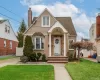 Cape Cod with a chimney, fence, brick siding, a front lawn, and a shingled roof Cape Cod with a chimney, fence, brick siding, a front lawn, and a shingled roof