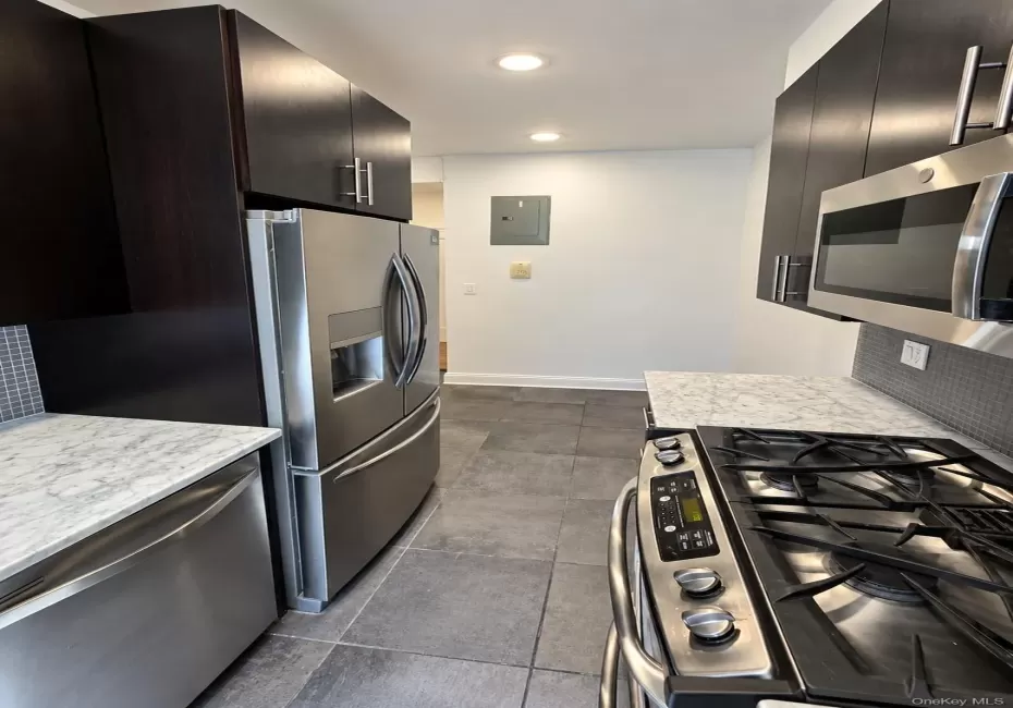 Kitchen featuring dark wood-finish cabinetry, stainless steel appliances, marble-finish countertops, and tile flooring Kitchen featuring dark wood-finish cabinetry, stainless steel appliances, marble-finish countertops, and tile flooring