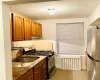 Kitchen featuring radiator heating unit, light tile patterned flooring, stainless steel appliances, backsplash, and under cabinet range hood Kitchen featuring radiator heating unit, light tile patterned flooring, stainless steel appliances, backsplash, and under cabinet range hood