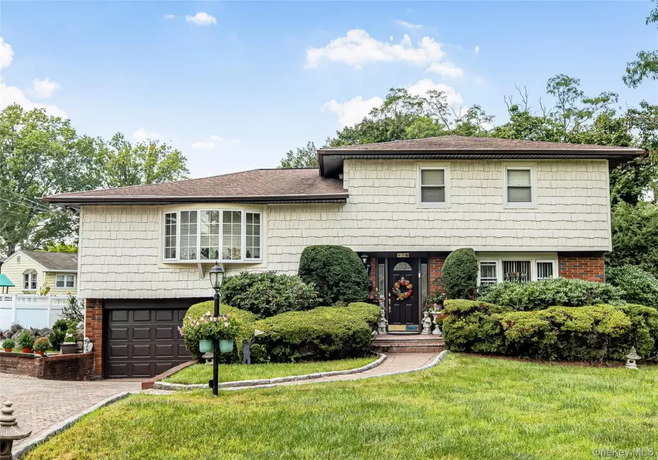 Split-level residence featuring brick and shake siding, an attached garage, a bay window, and a paver driveway Split-level residence featuring brick and shake siding, an attached garage, a bay window, and a paver driveway