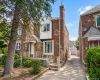 Brick and stone exterior with a prominent chimney, covered entry, front porch with railings, and a paved driveway leading to a detached garage Brick and stone exterior with a prominent chimney, covered entry, front porch with railings, and a paved driveway leading to a detached garage
