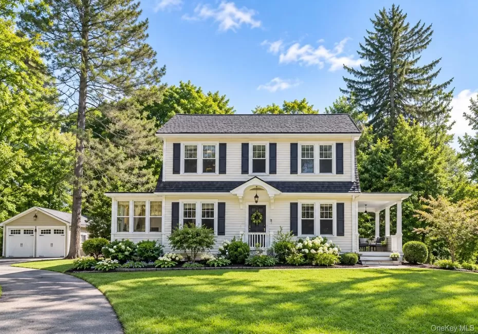 Two-story Colonial-style residence with white siding and dark shutters, featuring a covered front entry and a side porch Two-story Colonial-style residence with white siding and dark shutters, featuring a covered front entry and a side porch