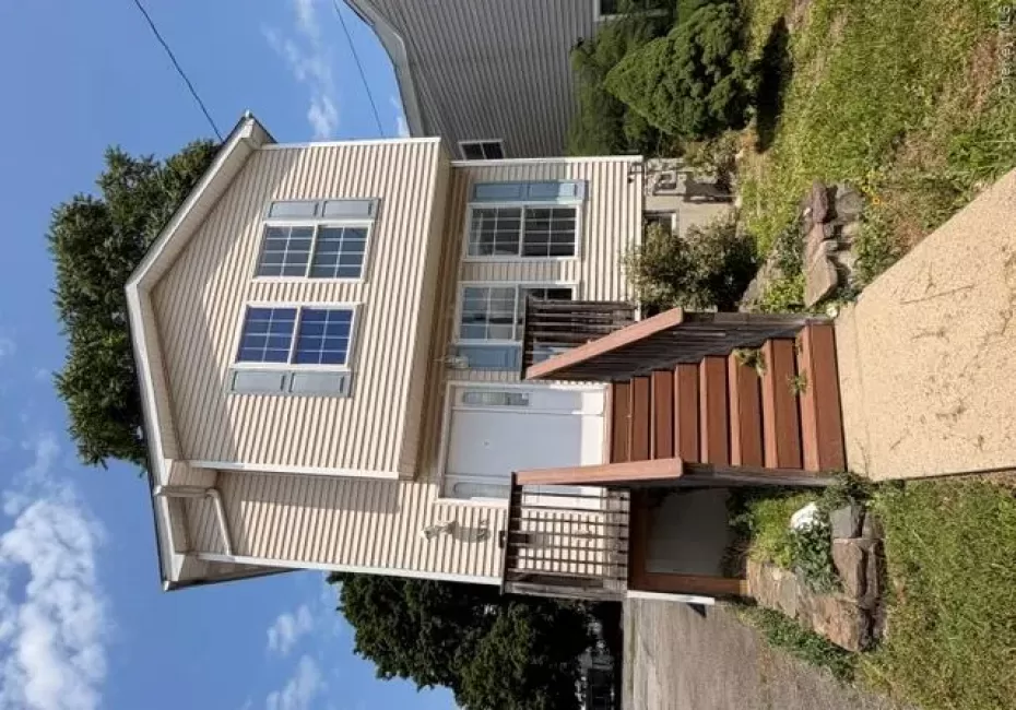 Two-story home with light-toned siding, a front entry deck, and a concrete pathway Two-story home with light-toned siding, a front entry deck, and a concrete pathway