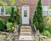 Entrance, Brick exterior featuring a white paneled entry door with glass inserts, flanked by decorative evergreens Entrance, Brick exterior featuring a white paneled entry door with glass inserts, flanked by decorative evergreens