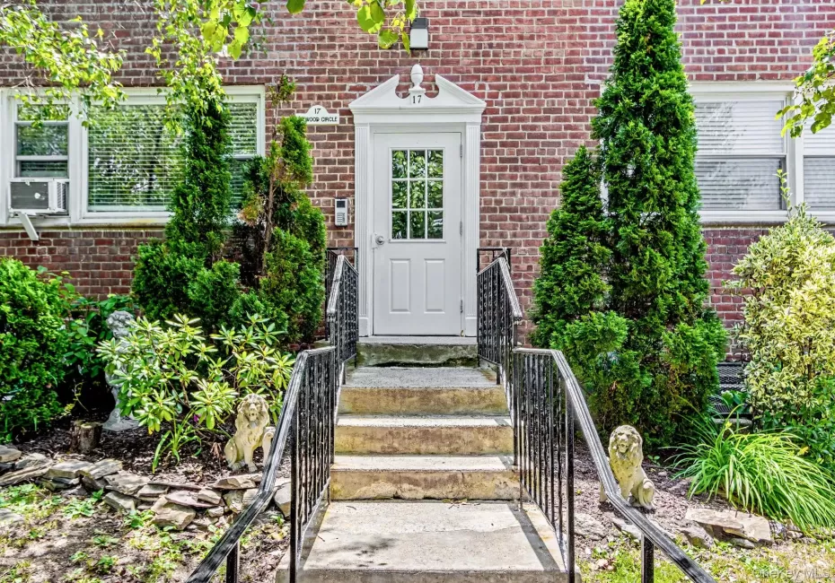 Entrance, Brick exterior featuring a white paneled entry door with glass inserts, flanked by decorative evergreens Entrance, Brick exterior featuring a white paneled entry door with glass inserts, flanked by decorative evergreens