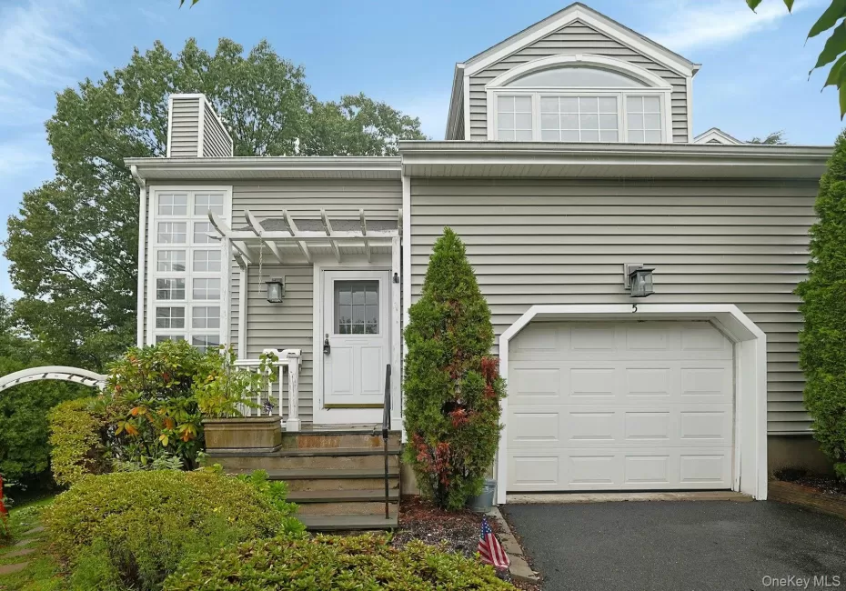 Siding exterior with a paneled garage door, arched window, and a white front entry door with an overhead pergola Siding exterior with a paneled garage door, arched window, and a white front entry door with an overhead pergola