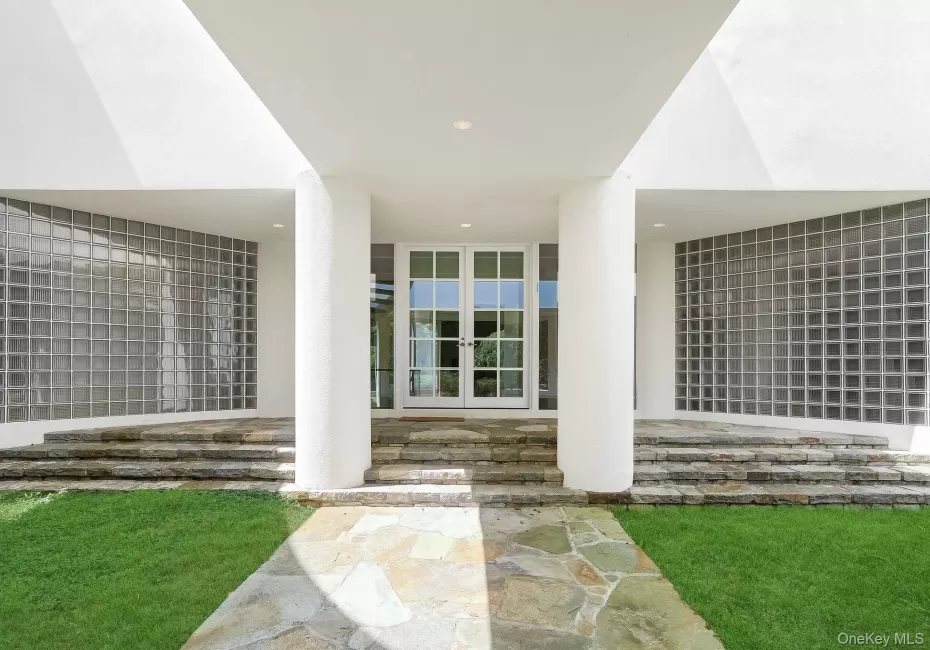 Oversized columns and elegant glass double doors frame a spectacular modern entry framed by curved glass-block privacy walls. Oversized columns and elegant glass double doors frame a spectacular modern entry framed by curved glass-block privacy walls.