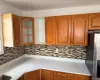 Warm wood cabinetry with decorative fronts, glass-front upper cabinet, linear mosaic tile backsplash, solid surface countertops, and stainless steel refrigerator Warm wood cabinetry with decorative fronts, glass-front upper cabinet, linear mosaic tile backsplash, solid surface countertops, and stainless steel refrigerator