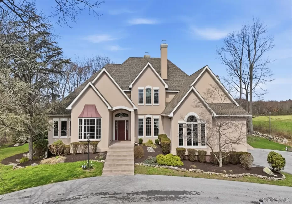 The property features a stucco exterior, a prominent front entrance with a dark red door and steps, and a bay window with a distinctive copper-colored awning The property features a stucco exterior, a prominent front entrance with a dark red door and steps, and a bay window with a distinctive copper-colored awning