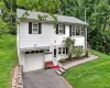 White siding exterior with black shutters, attached garage, paved driveway, stone retaining wall, and a paver walkway White siding exterior with black shutters, attached garage, paved driveway, stone retaining wall, and a paver walkway