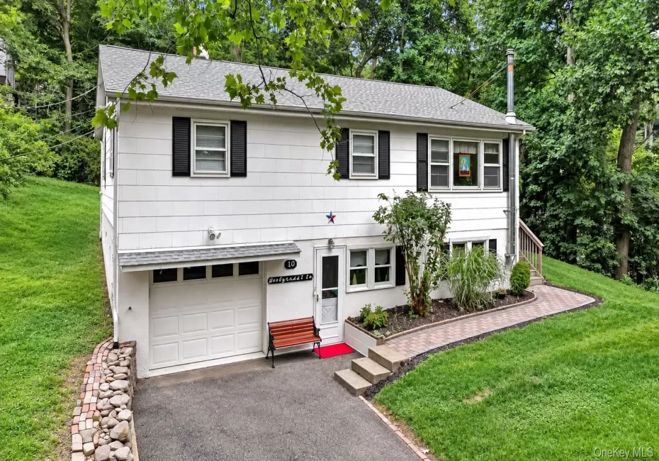 White siding exterior with black shutters, attached garage, paved driveway, stone retaining wall, and a paver walkway White siding exterior with black shutters, attached garage, paved driveway, stone retaining wall, and a paver walkway