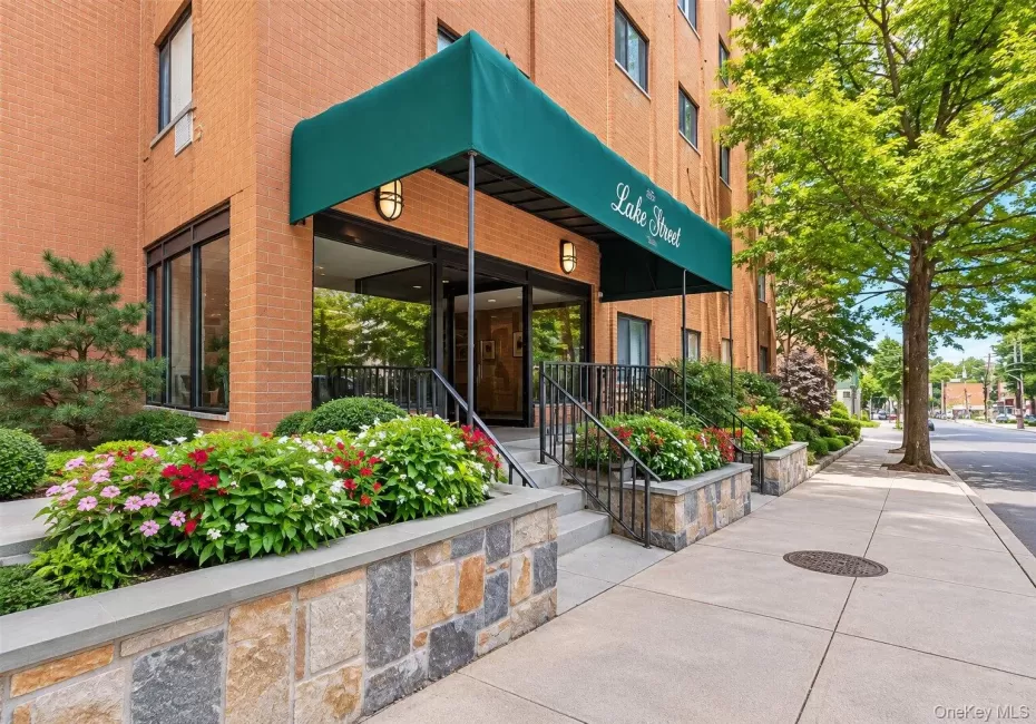 Brick facade building featuring a green awning, stone-clad planters, wrought iron railings, and extensive landscaping Brick facade building featuring a green awning, stone-clad planters, wrought iron railings, and extensive landscaping