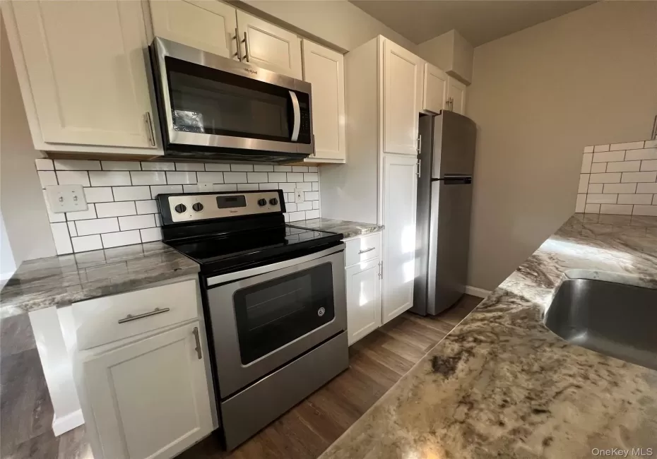 Kitchen featuring white cabinetry, stainless steel appliances, patterned countertops, white subway tile backsplash, and wood-finish flooring Kitchen featuring white cabinetry, stainless steel appliances, patterned countertops, white subway tile backsplash, and wood-finish flooring
