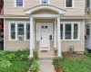 Columned portico entrance with a concrete pathway, flanked by garden beds, and light-toned siding Columned portico entrance with a concrete pathway, flanked by garden beds, and light-toned siding