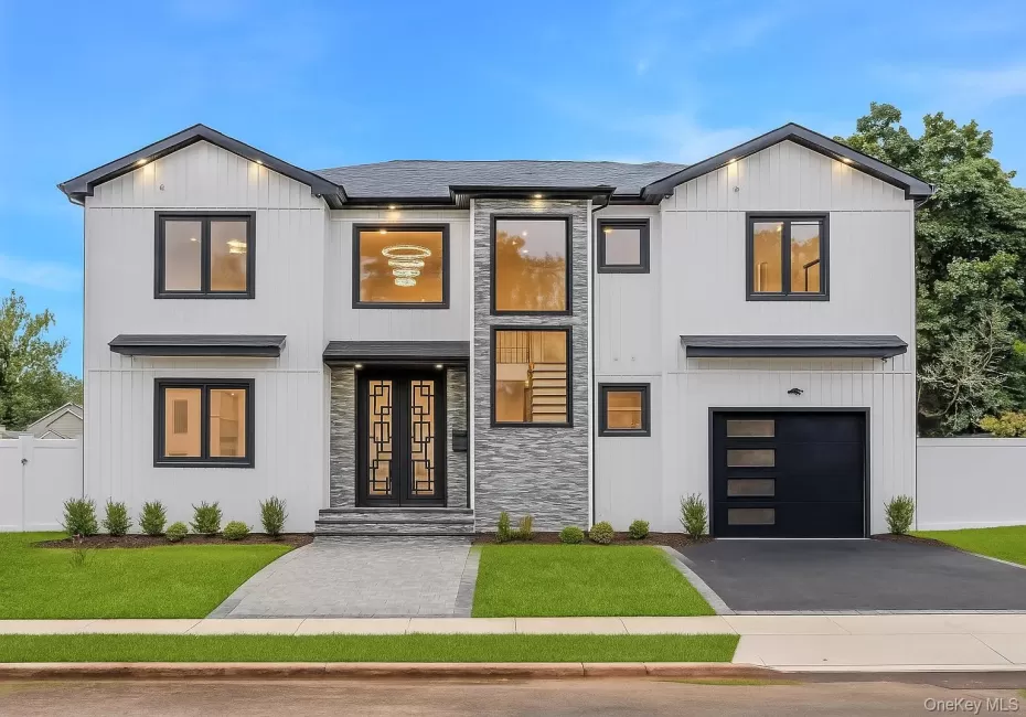 Contemporary exterior featuring white vertical siding, black-framed windows, a two-car garage with a modern door, a stone-clad entry, and a paved walkway Contemporary exterior featuring white vertical siding, black-framed windows, a two-car garage with a modern door, a stone-clad entry, and a paved walkway