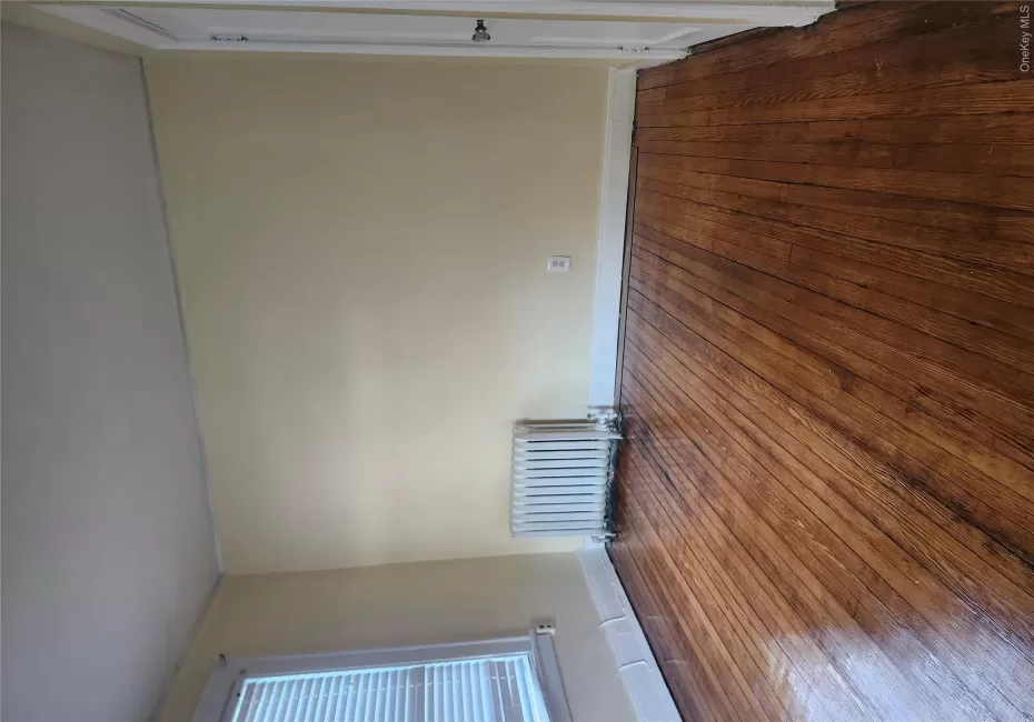Hardwood flooring, painted walls, baseboard trim, window with blinds, and a radiator Hardwood flooring, painted walls, baseboard trim, window with blinds, and a radiator