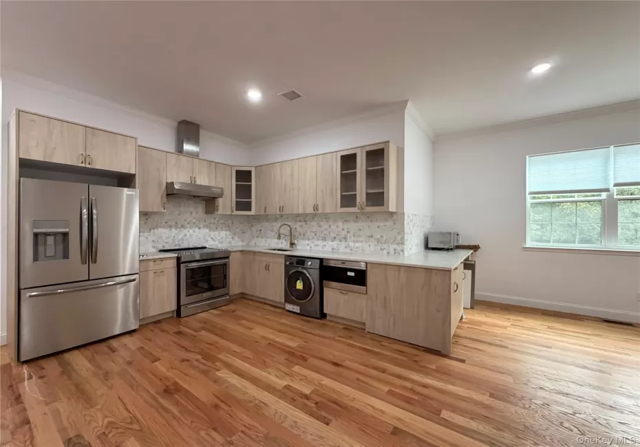 Kitchen featuring stainless steel appliances, wood-finish cabinetry, light-toned countertops, and a full tile backsplash Kitchen featuring stainless steel appliances, wood-finish cabinetry, light-toned countertops, and a full tile backsplash