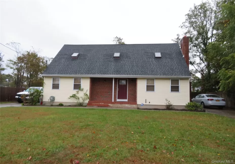 Exterior featuring light-colored siding, a dark shingle roof with multiple skylights, a brick facade, and a prominent brick chimney Exterior featuring light-colored siding, a dark shingle roof with multiple skylights, a brick facade, and a prominent brick chimney