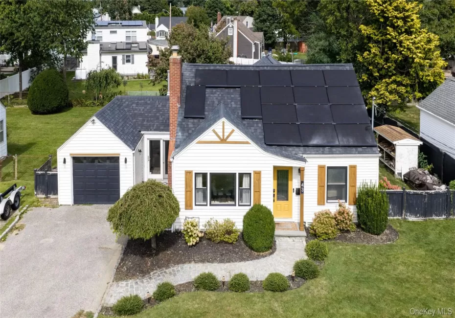 White siding exterior with a dark shingled roof, featuring solar panels and a brick chimney White siding exterior with a dark shingled roof, featuring solar panels and a brick chimney