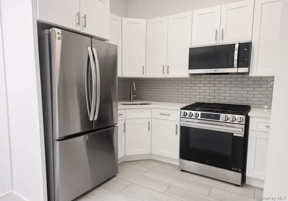 Kitchen featuring white shaker cabinetry, stainless steel appliances, light-toned countertops, subway tile backsplash, and light wood-finish flooring Kitchen featuring white shaker cabinetry, stainless steel appliances, light-toned countertops, subway tile backsplash, and light wood-finish flooring
