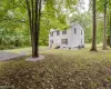 Siding exterior with black window shutters, partial wood porch, mature trees, and a gravel tree ring Siding exterior with black window shutters, partial wood porch, mature trees, and a gravel tree ring