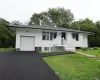 White exterior siding with dark trim, attached garage, front porch with white railing, paved driveway, and grass lawn White exterior siding with dark trim, attached garage, front porch with white railing, paved driveway, and grass lawn