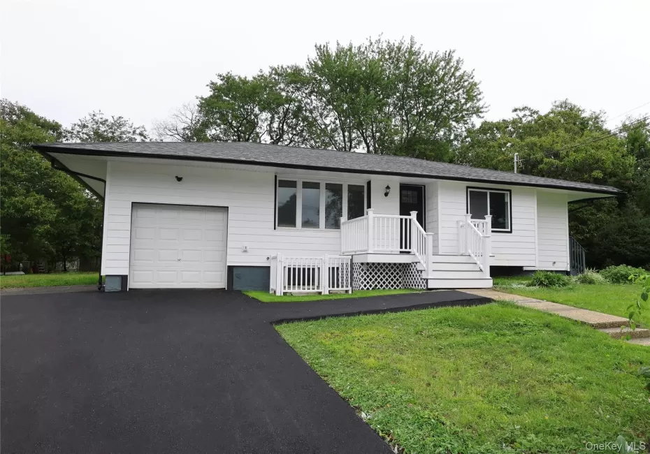 White exterior siding with dark trim, attached garage, front porch with white railing, paved driveway, and grass lawn White exterior siding with dark trim, attached garage, front porch with white railing, paved driveway, and grass lawn