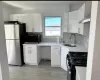 Modern kitchen featuring white cabinetry, light-toned countertops, a stainless steel refrigerator, a gas range, and a tile backsplash Modern kitchen featuring white cabinetry, light-toned countertops, a stainless steel refrigerator, a gas range, and a tile backsplash