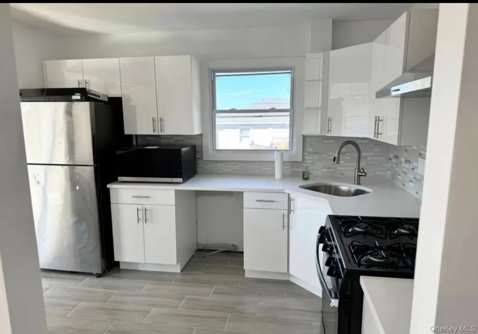 Modern kitchen featuring white cabinetry, light-toned countertops, a stainless steel refrigerator, a gas range, and a tile backsplash Modern kitchen featuring white cabinetry, light-toned countertops, a stainless steel refrigerator, a gas range, and a tile backsplash