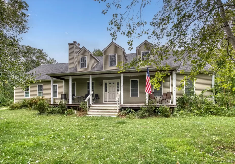 Expansive front lawn leading to a welcoming covered porch, dormer windows, and a prominent chimney Expansive front lawn leading to a welcoming covered porch, dormer windows, and a prominent chimney
