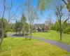 Expansive grassy lawn with established landscaping and mature trees and colonial style house with fencing. Expansive grassy lawn with established landscaping and mature trees and colonial style house with fencing.