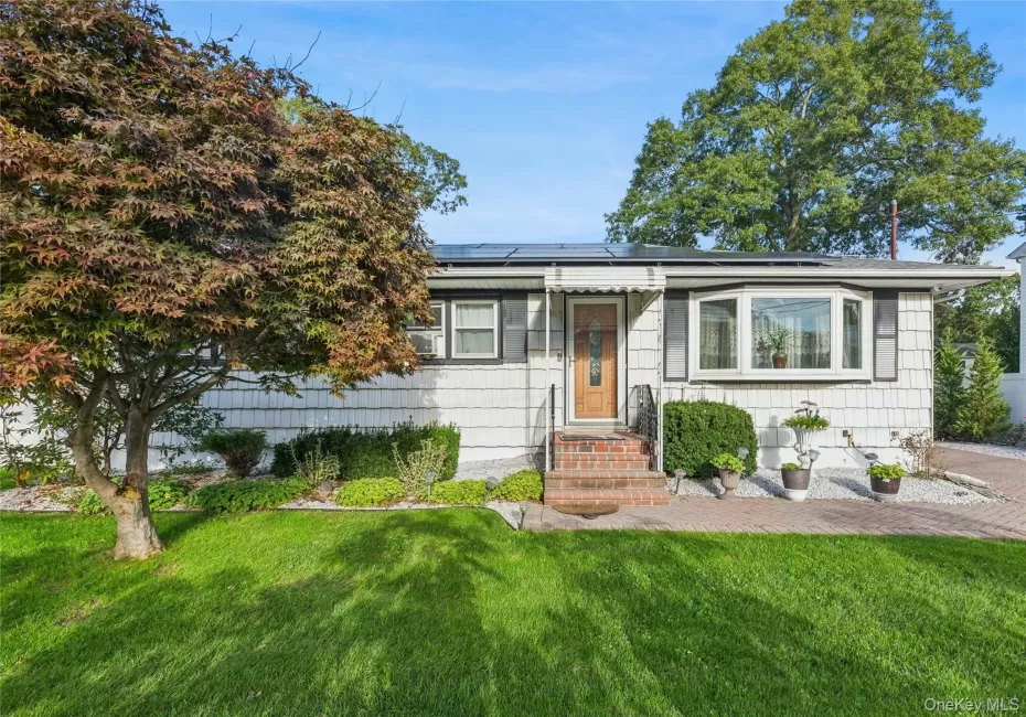 White shingle siding, bay window, front entry with brick steps, solar panel installation, and mature front yard landscaping White shingle siding, bay window, front entry with brick steps, solar panel installation, and mature front yard landscaping