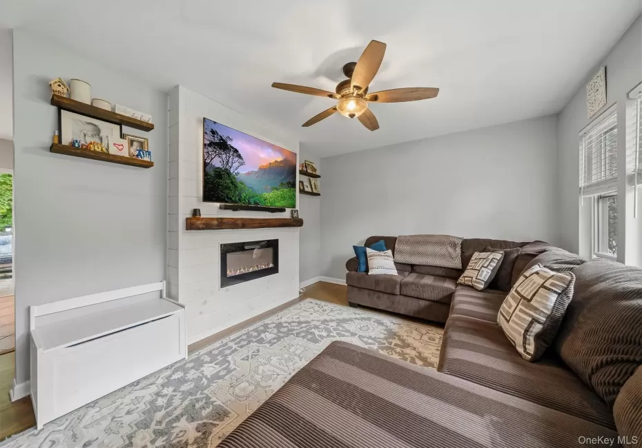 Living space with a shiplap feature wall, integrated electric fireplace, wood-finish mantel, and ceiling fan Living space with a shiplap feature wall, integrated electric fireplace, wood-finish mantel, and ceiling fan