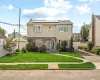 Two-story residence featuring a shingled exterior and stone facade, solar panels, a paved driveway, and a front lawn with a concrete pathway Two-story residence featuring a shingled exterior and stone facade, solar panels, a paved driveway, and a front lawn with a concrete pathway