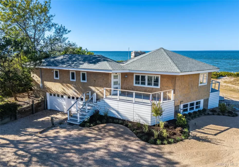 View of front of property featuring dirt driveway, roof with shingles, an attached garage, stairs, and a water view View of front of property featuring dirt driveway, roof with shingles, an attached garage, stairs, and a water view