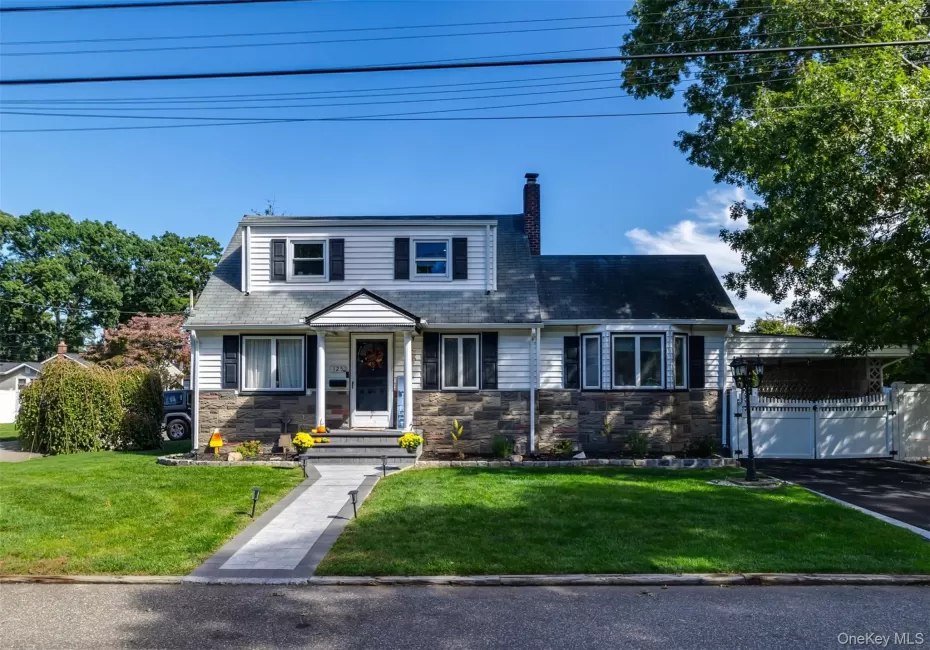 Cape Cod style residence featuring a stone and siding facade, a paved driveway, and a front walkway with integrated lighting Cape Cod style residence featuring a stone and siding facade, a paved driveway, and a front walkway with integrated lighting