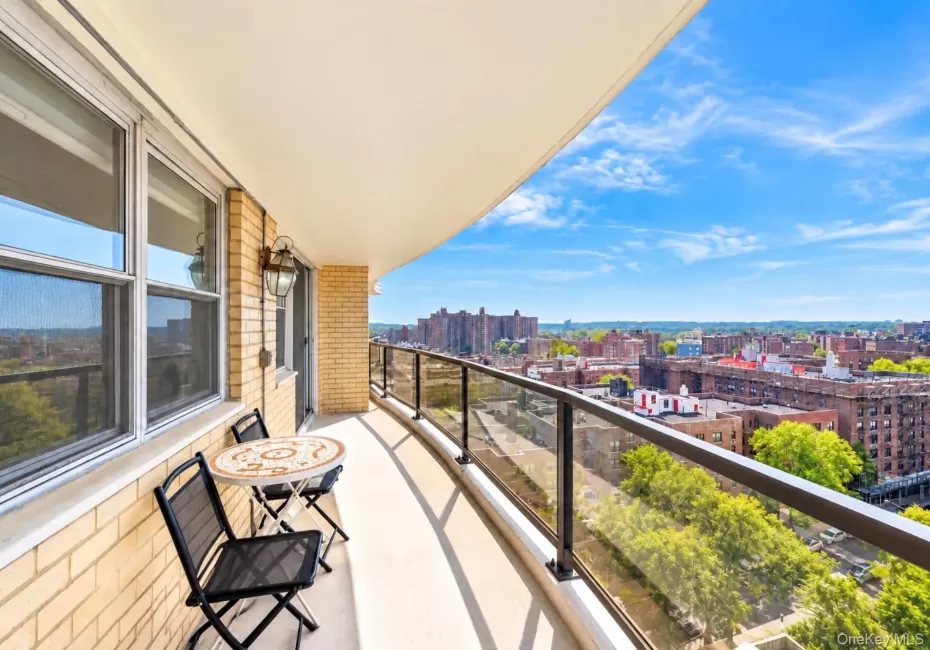 Expansive balcony featuring a glass railing, brick exterior, and outdoor wall sconce Expansive balcony featuring a glass railing, brick exterior, and outdoor wall sconce