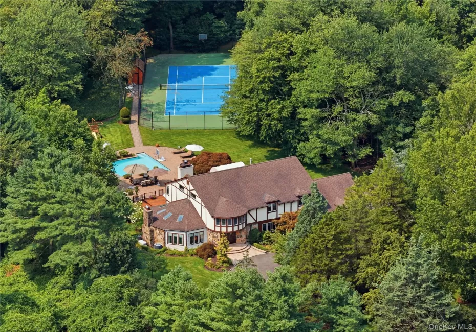 Tudor-style residence set amidst lush trees, featuring mahogany decking, stone patio, tennis court, and swimming pool. Tudor-style residence set amidst lush trees, featuring mahogany decking, stone patio, tennis court, and swimming pool.