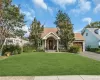 Pitched roof with asphalt shingles, stone facade entrance, attached garage with wood-finish door, paved driveway, and established landscaping Pitched roof with asphalt shingles, stone facade entrance, attached garage with wood-finish door, paved driveway, and established landscaping