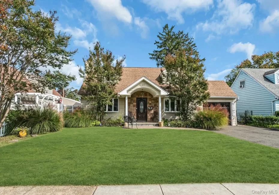 Pitched roof with asphalt shingles, stone facade entrance, attached garage with wood-finish door, paved driveway, and established landscaping Pitched roof with asphalt shingles, stone facade entrance, attached garage with wood-finish door, paved driveway, and established landscaping