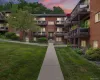 Brick exterior building with multiple private balconies featuring dark railings, surrounded by mature landscaping and a concrete pathway Brick exterior building with multiple private balconies featuring dark railings, surrounded by mature landscaping and a concrete pathway