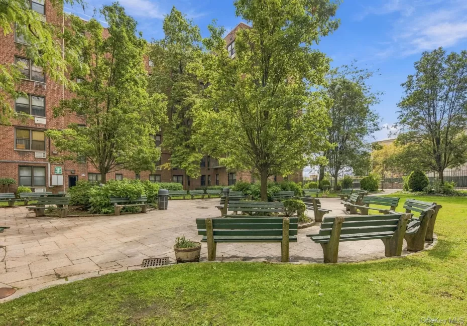 Landscaped courtyard featuring mature trees, green lawn, paved walking paths, and multiple park benches Landscaped courtyard featuring mature trees, green lawn, paved walking paths, and multiple park benches