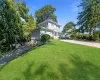 Two-story residence featuring grey horizontal lap siding, a front entry portico with dual columns, a gravel driveway, and mature landscaping Two-story residence featuring grey horizontal lap siding, a front entry portico with dual columns, a gravel driveway, and mature landscaping