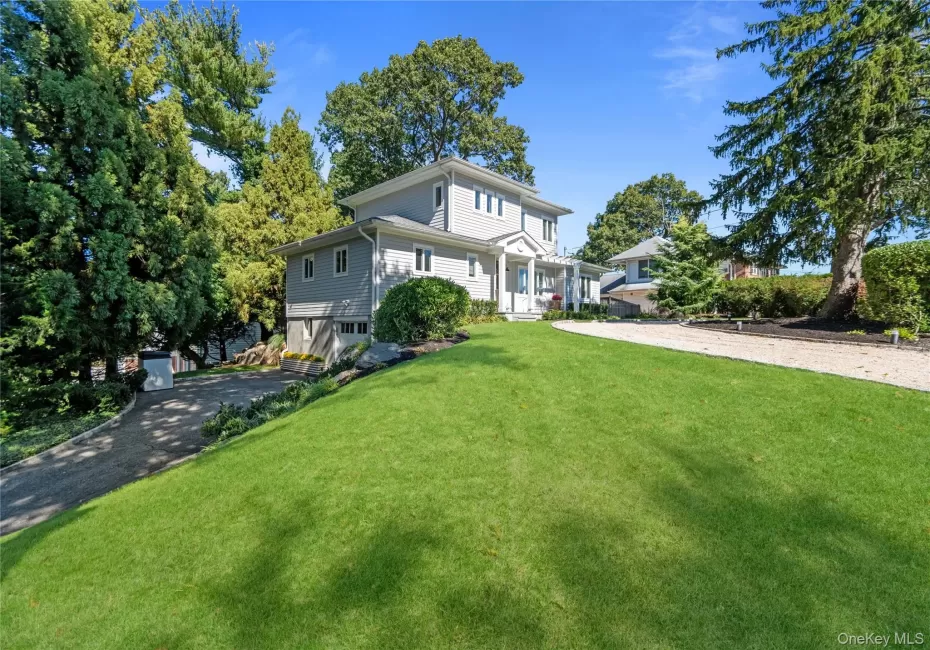 Two-story residence featuring grey horizontal lap siding, a front entry portico with dual columns, a gravel driveway, and mature landscaping Two-story residence featuring grey horizontal lap siding, a front entry portico with dual columns, a gravel driveway, and mature landscaping
