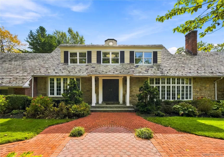 Stone and clapboard exterior featuring a covered entryway with columns, a shingled roof with a chimney, and a multi-patterned brick walkway Stone and clapboard exterior featuring a covered entryway with columns, a shingled roof with a chimney, and a multi-patterned brick walkway
